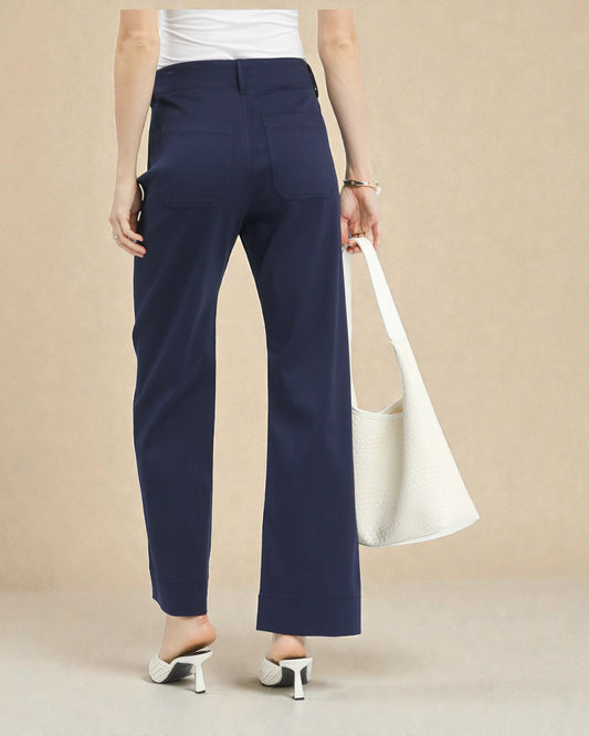 Person wearing navy pants holding a white bag against a beige background