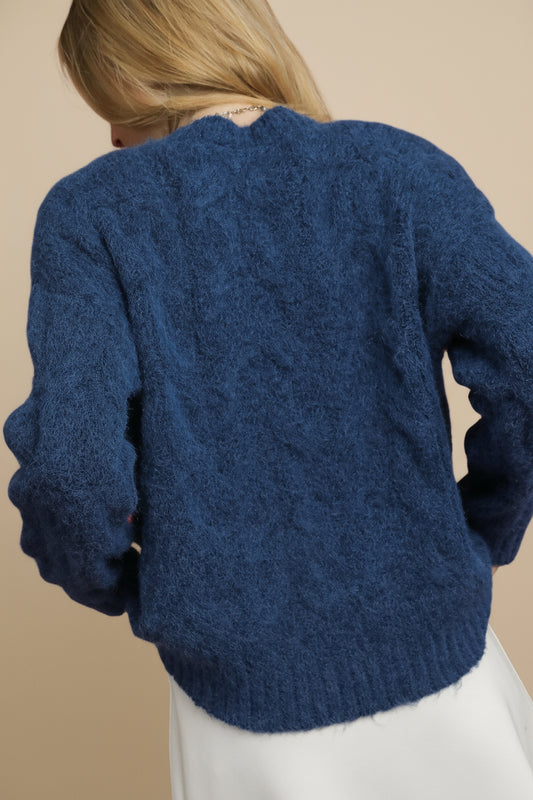 Blue knitted sweater worn by a person on a plain background