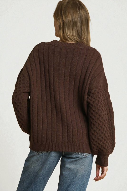 Person wearing a brown knitted sweater and blue jeans on a white background