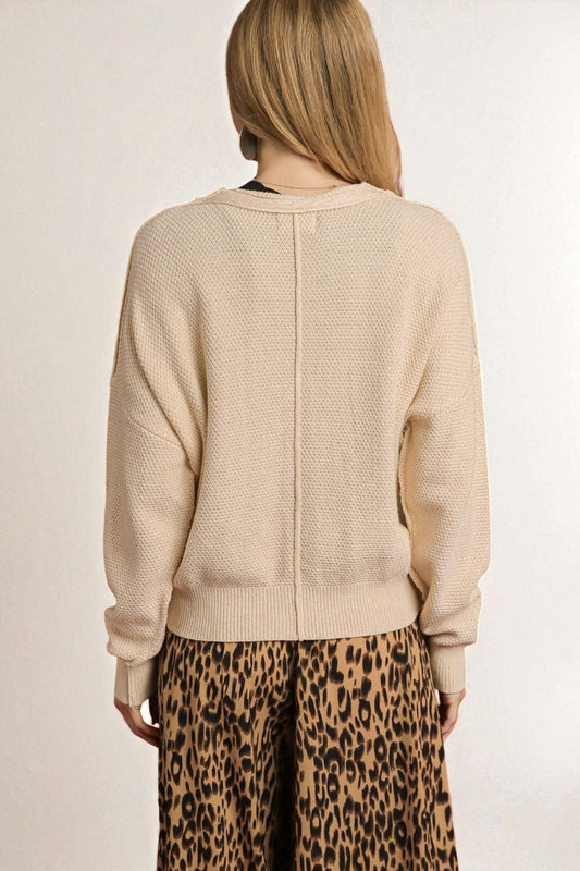 Person wearing a beige textured sweater and leopard print pants on a plain background