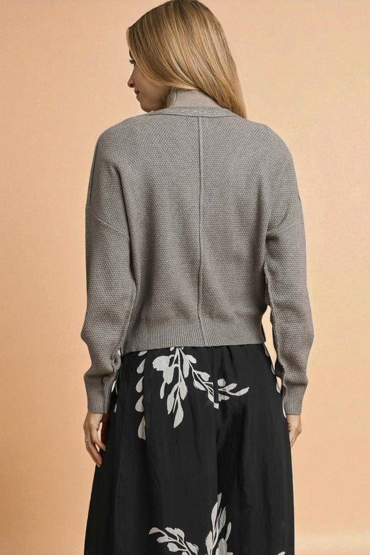 Woman wearing a gray textured cardigan over a black dress with white floral patterns on a beige background