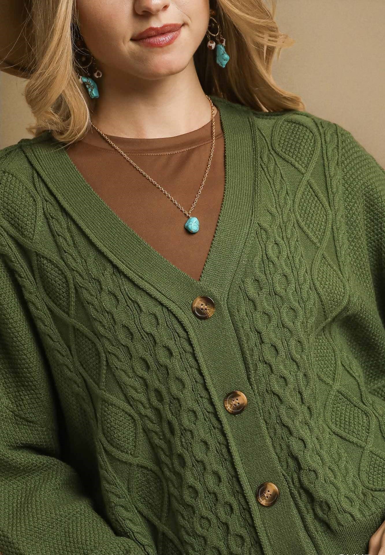 Green cable knit cardigan worn by a person, with a focus on the texture and design.
