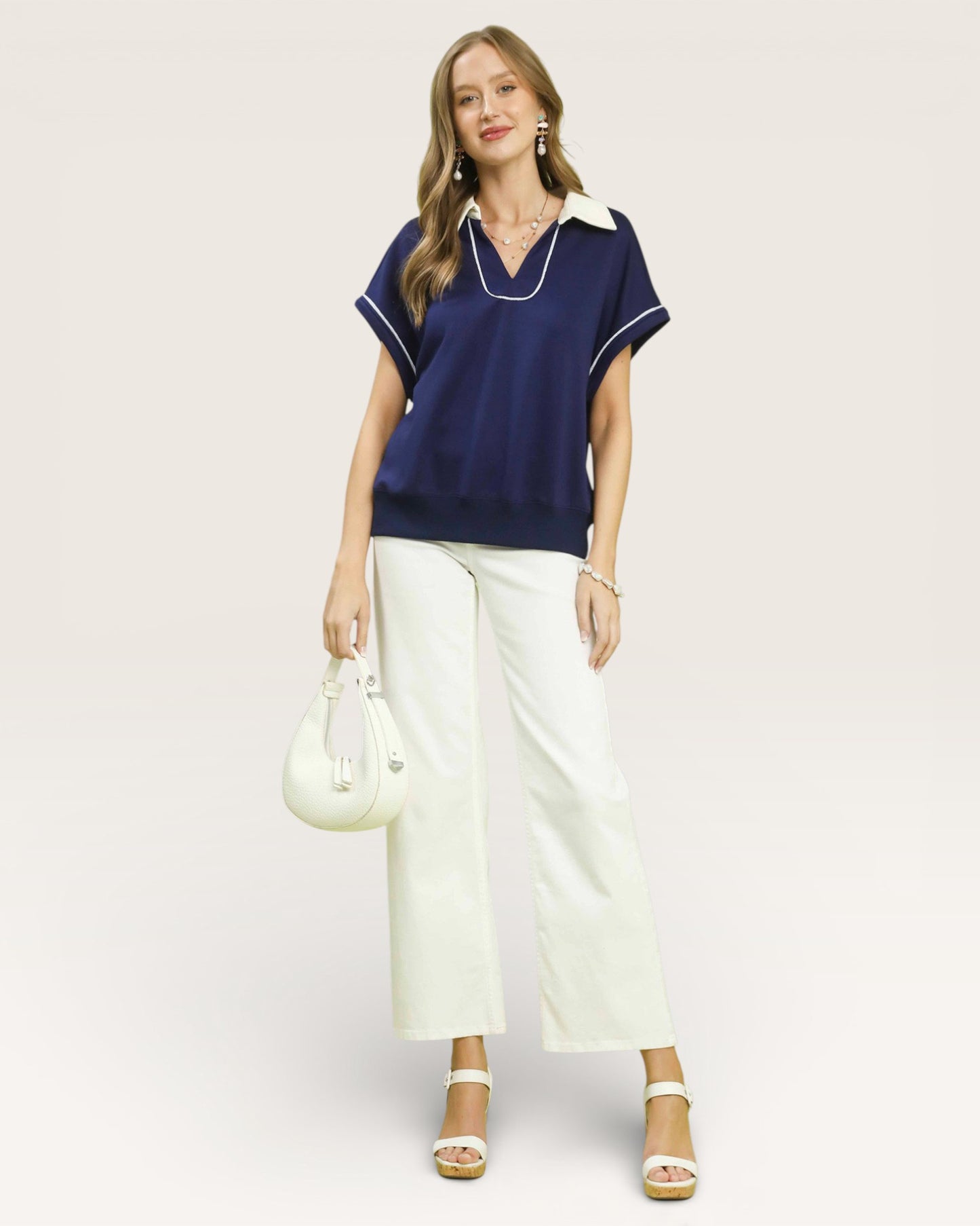 Woman wearing a navy top and white pants with a white background