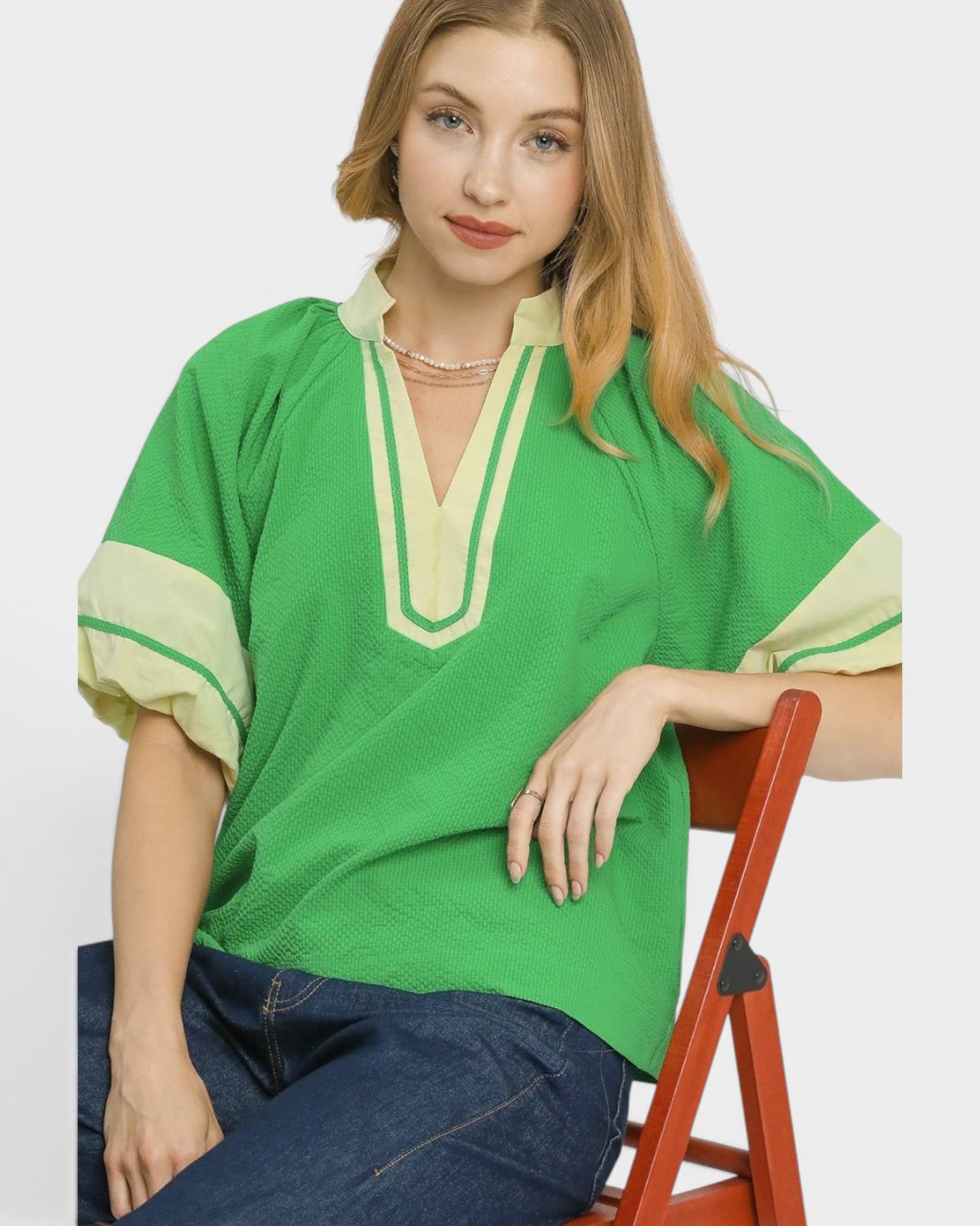 Woman wearing a green and beige top sitting on a red chair against a white background