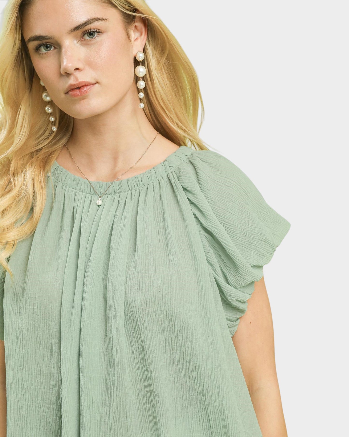 Woman wearing a light green dress with ruffled sleeves on a white background