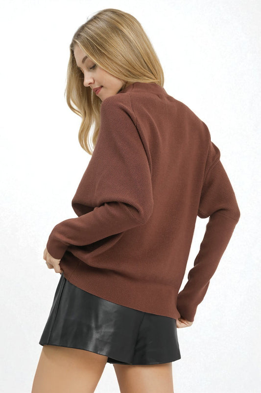 Woman wearing a brown sweater and black leather shorts on a white background
