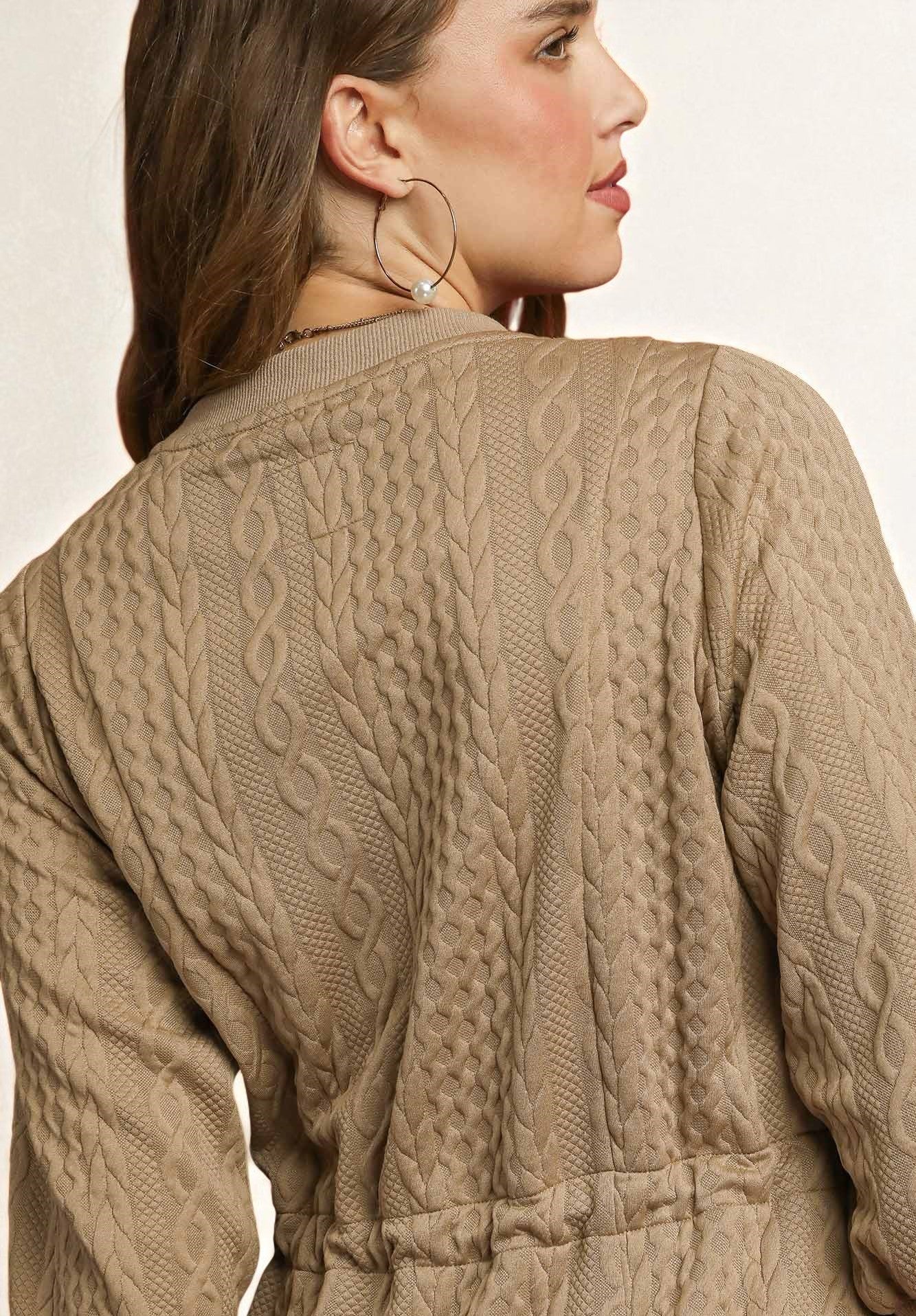 Close-up of a person wearing a beige cable knit cardigan on a plain background