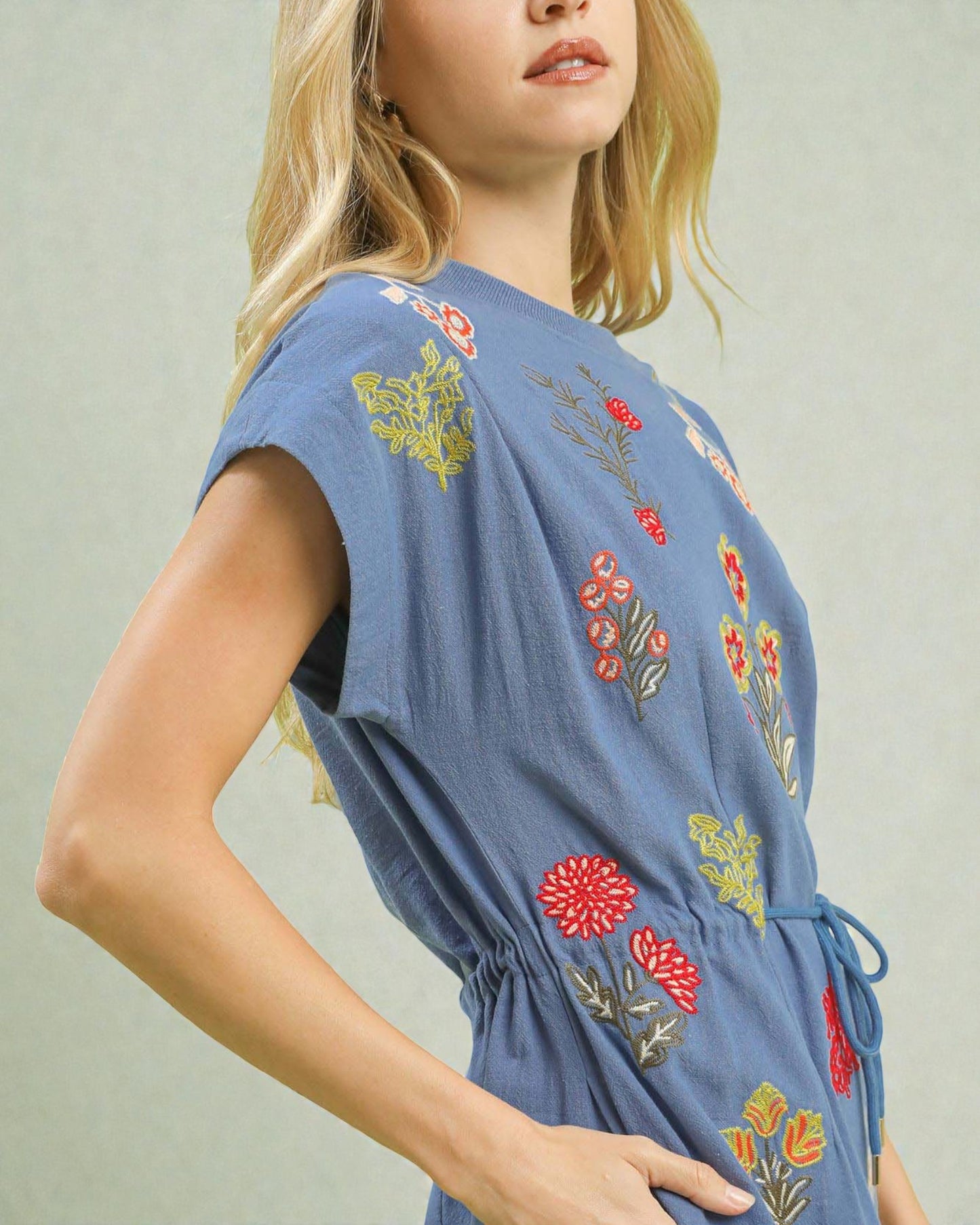 Woman wearing a blue dress with floral embroidery on a plain background