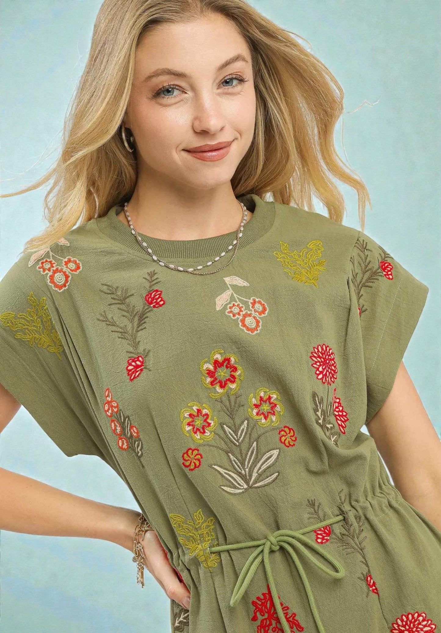 Woman wearing a green dress with floral embroidery against a light blue background