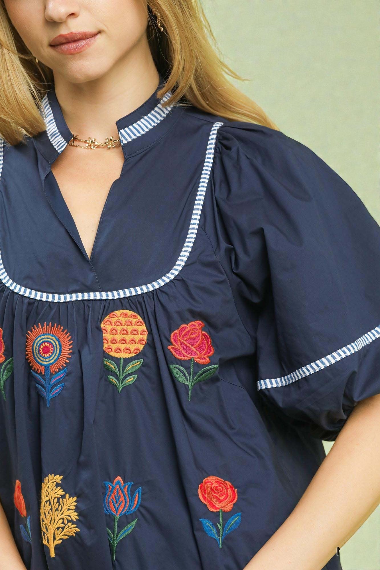 Navy blue blouse with colorful floral embroidery on a light green background