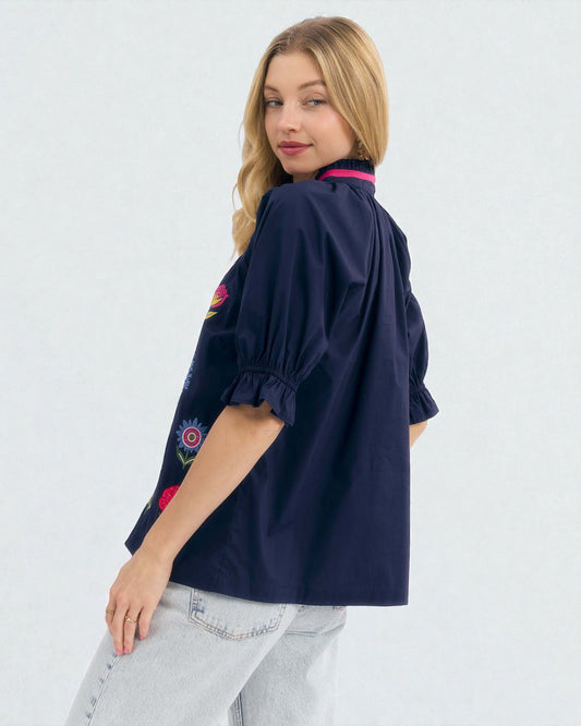 Woman wearing a navy blue blouse with floral embroidery on a white background