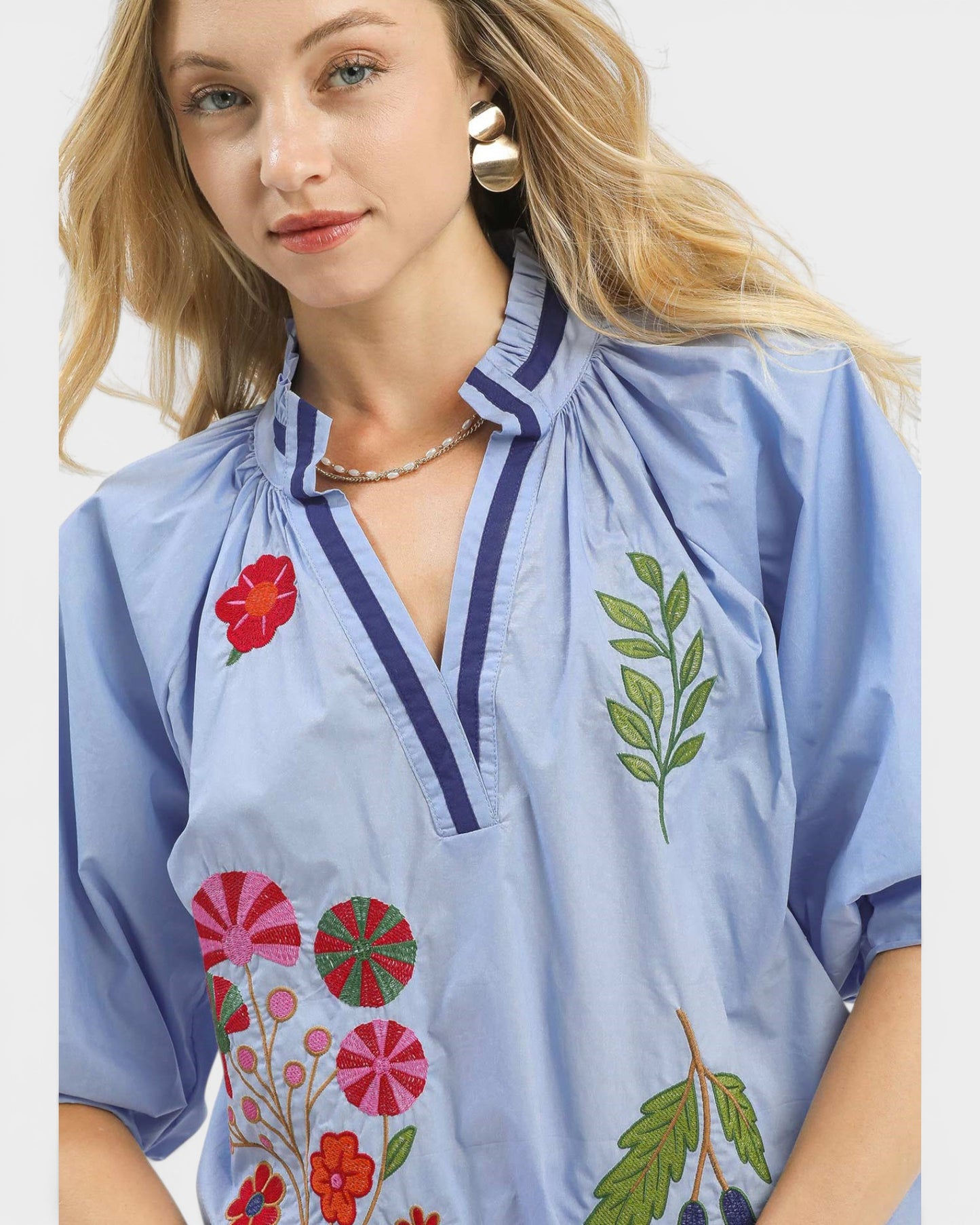 Woman wearing a blue blouse with floral embroidery on a plain background