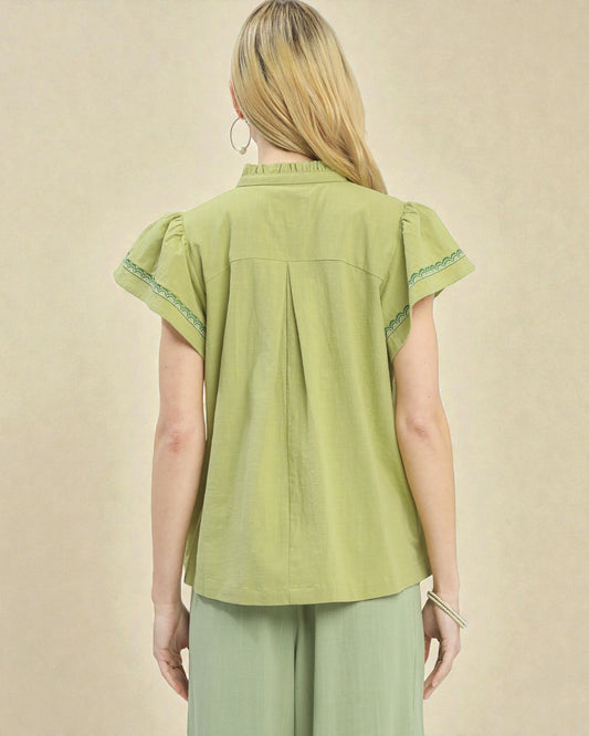 Woman wearing a green blouse with embroidered details on a beige background