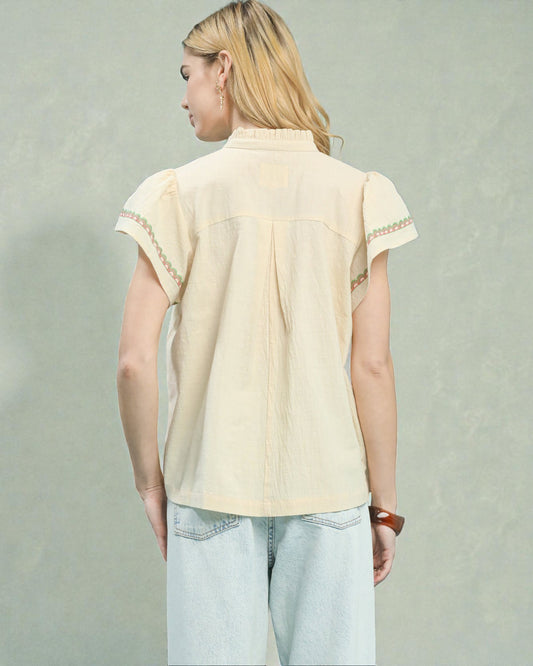 Person wearing a beige blouse with lace details on a plain background