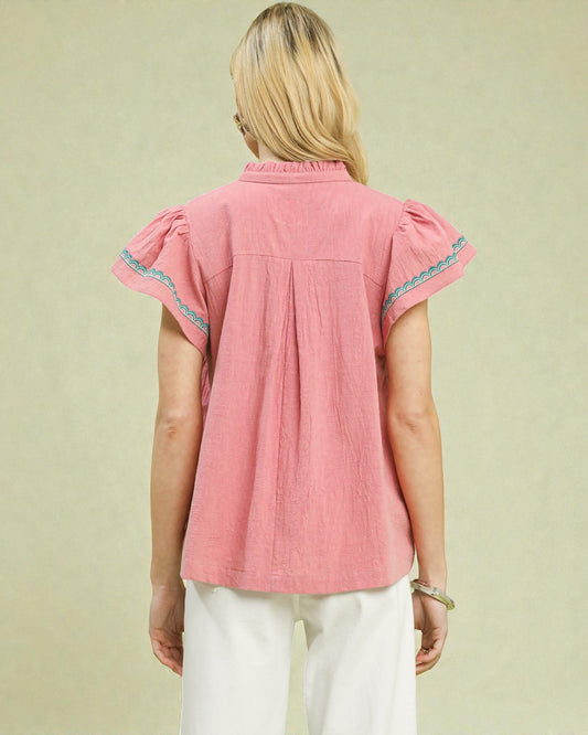 Woman wearing a pink blouse with lace trim on a beige background