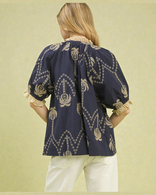 Woman wearing a navy blue blouse with gold patterns on a light green background