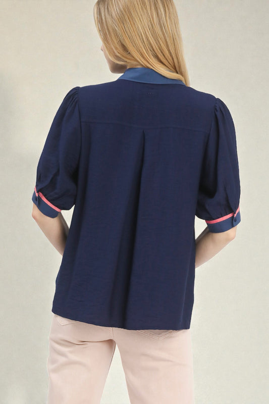 Navy blouse with pink trim worn by a person on a neutral background