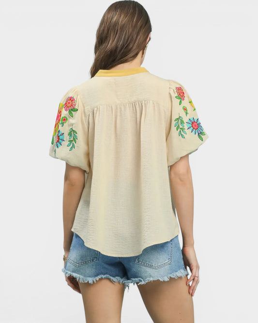 Woman wearing a beige blouse with floral embroidery on sleeves against a white background
