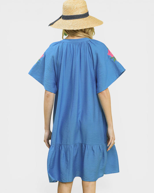 Woman wearing a blue dress with floral sleeves and a straw hat on a light gray background