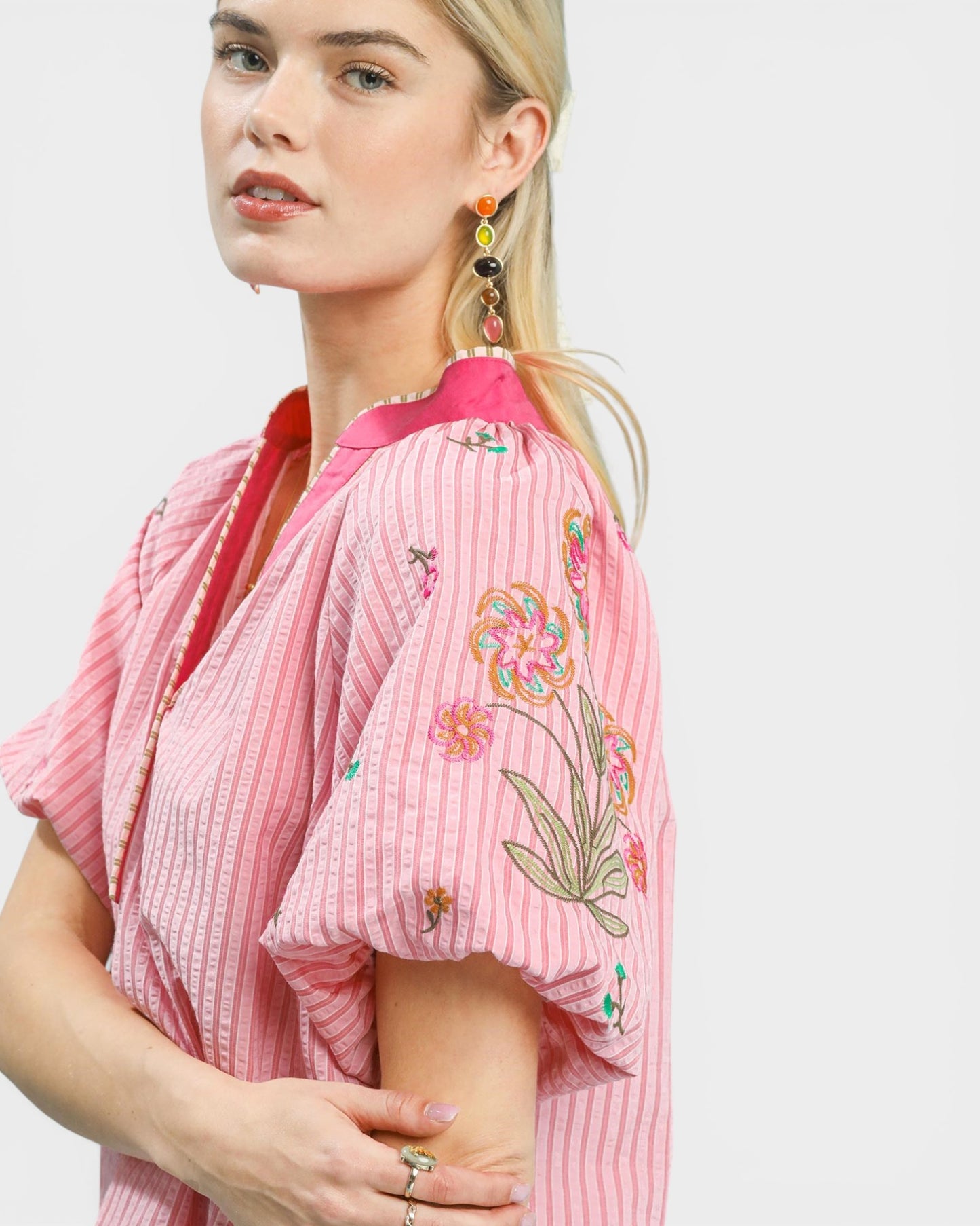 Woman wearing a pink embroidered blouse with a plain background