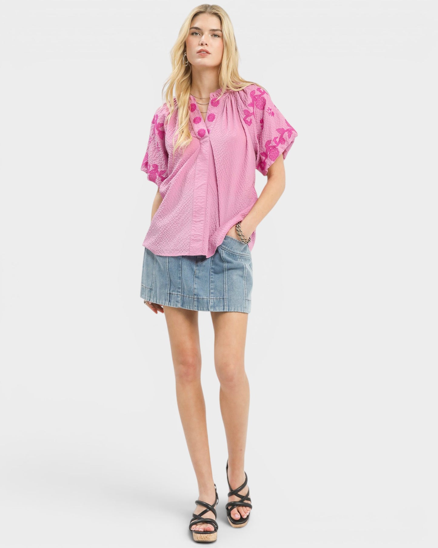 Woman wearing a pink blouse with floral patterns and a denim skirt on a white background