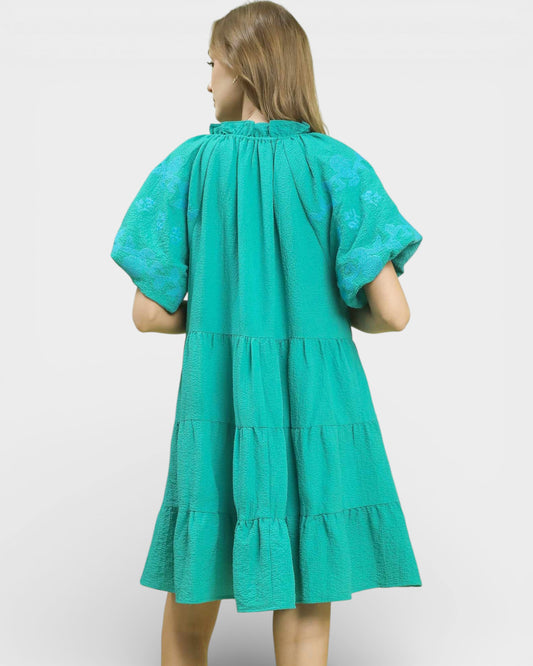 Woman wearing a teal dress with short sleeves and ruffled layers on a white background