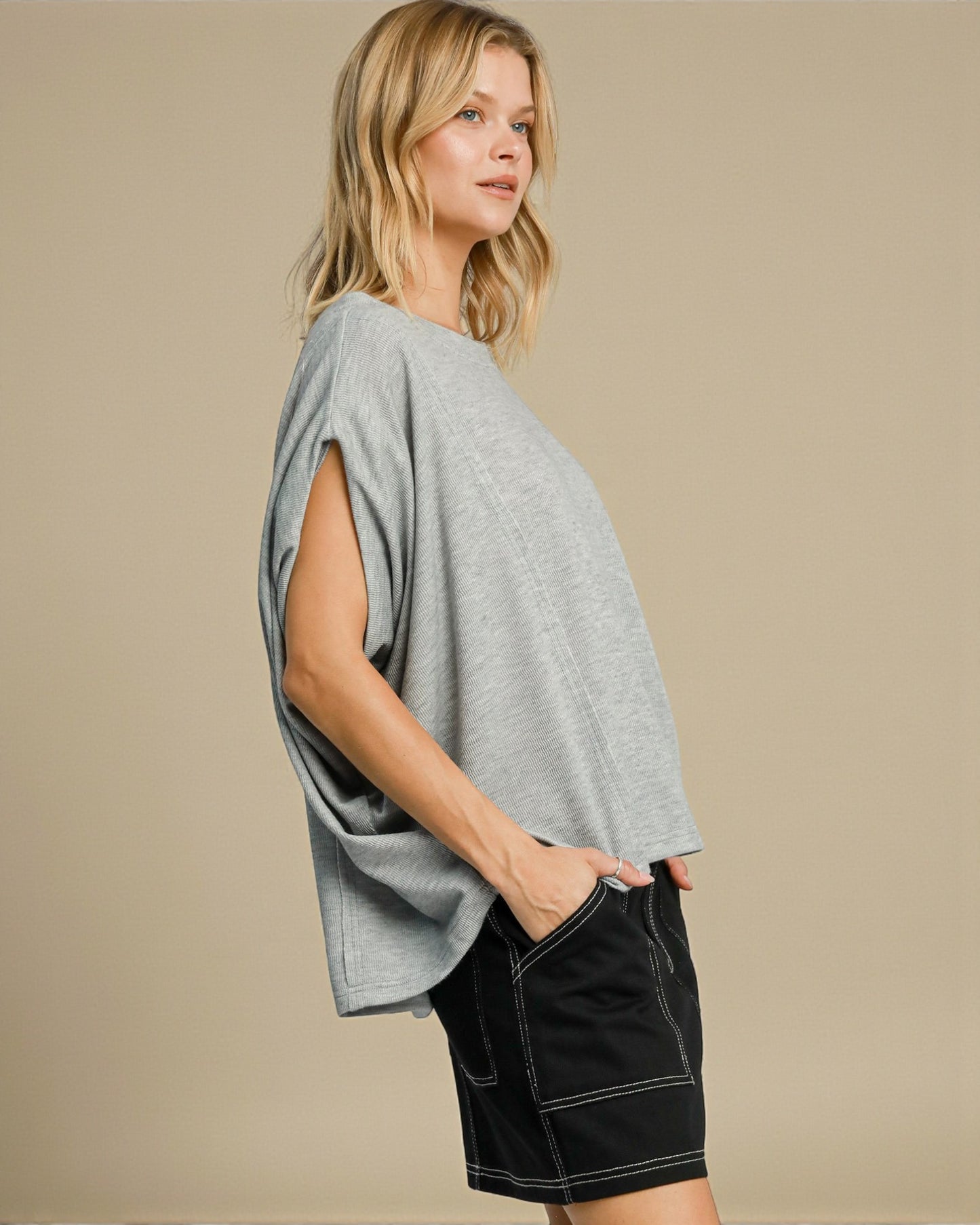 Woman wearing a gray oversized top and black shorts on a beige background