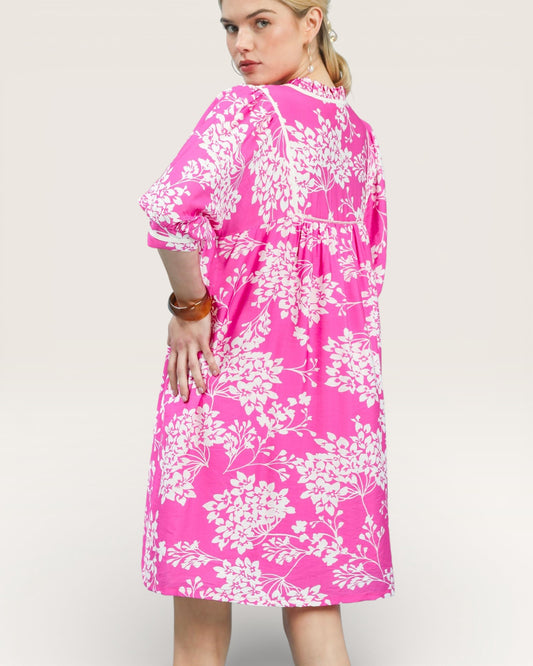 Woman wearing a pink dress with white floral pattern on a plain background
