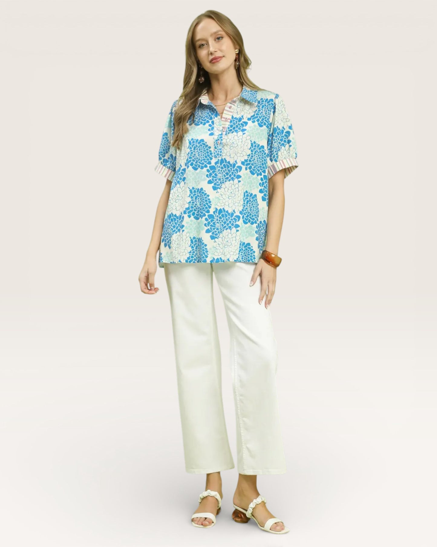 Woman wearing a blue floral blouse and white pants on a light pink background