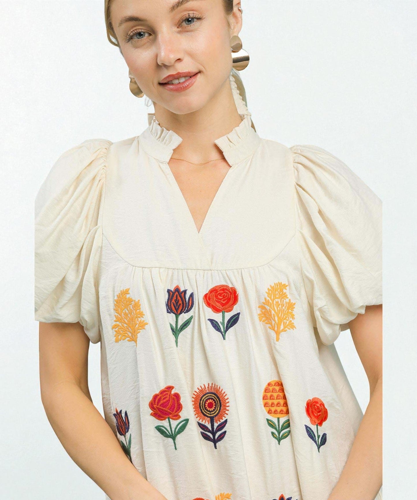 Woman wearing a cream-colored blouse with floral embroidery on a white background