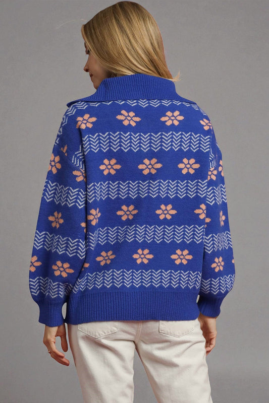 Person wearing a blue sweater with pink floral patterns on a gray background