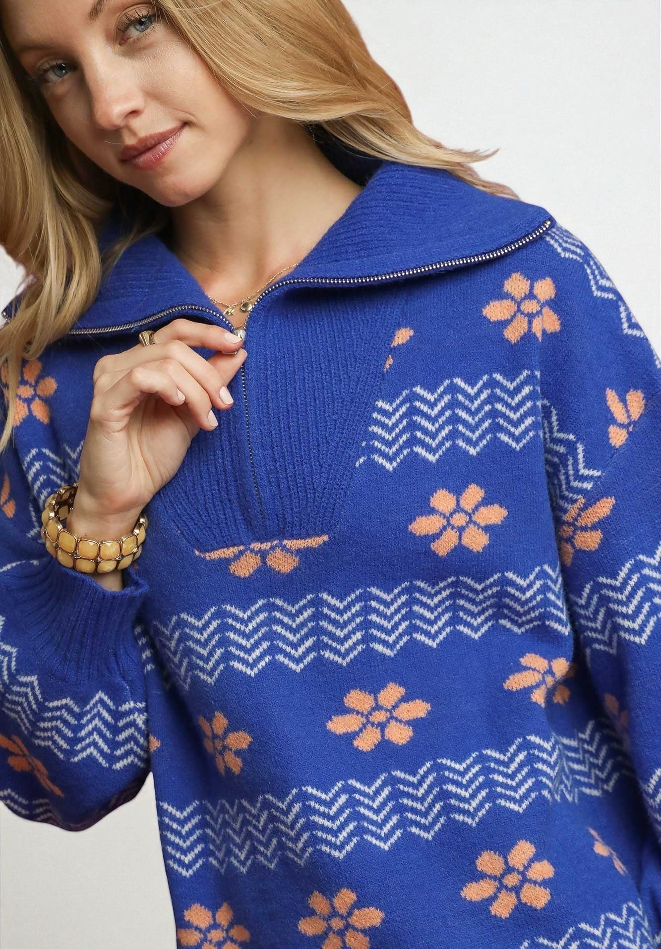 Woman wearing a blue sweater with orange floral patterns on a plain background