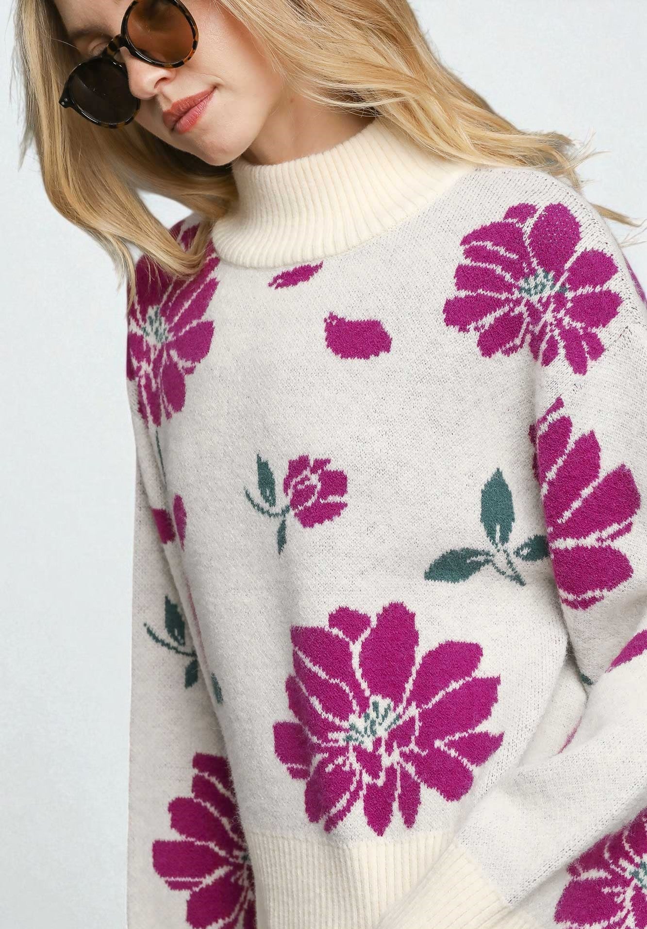 Woman wearing a cream sweater with pink floral patterns on a white background