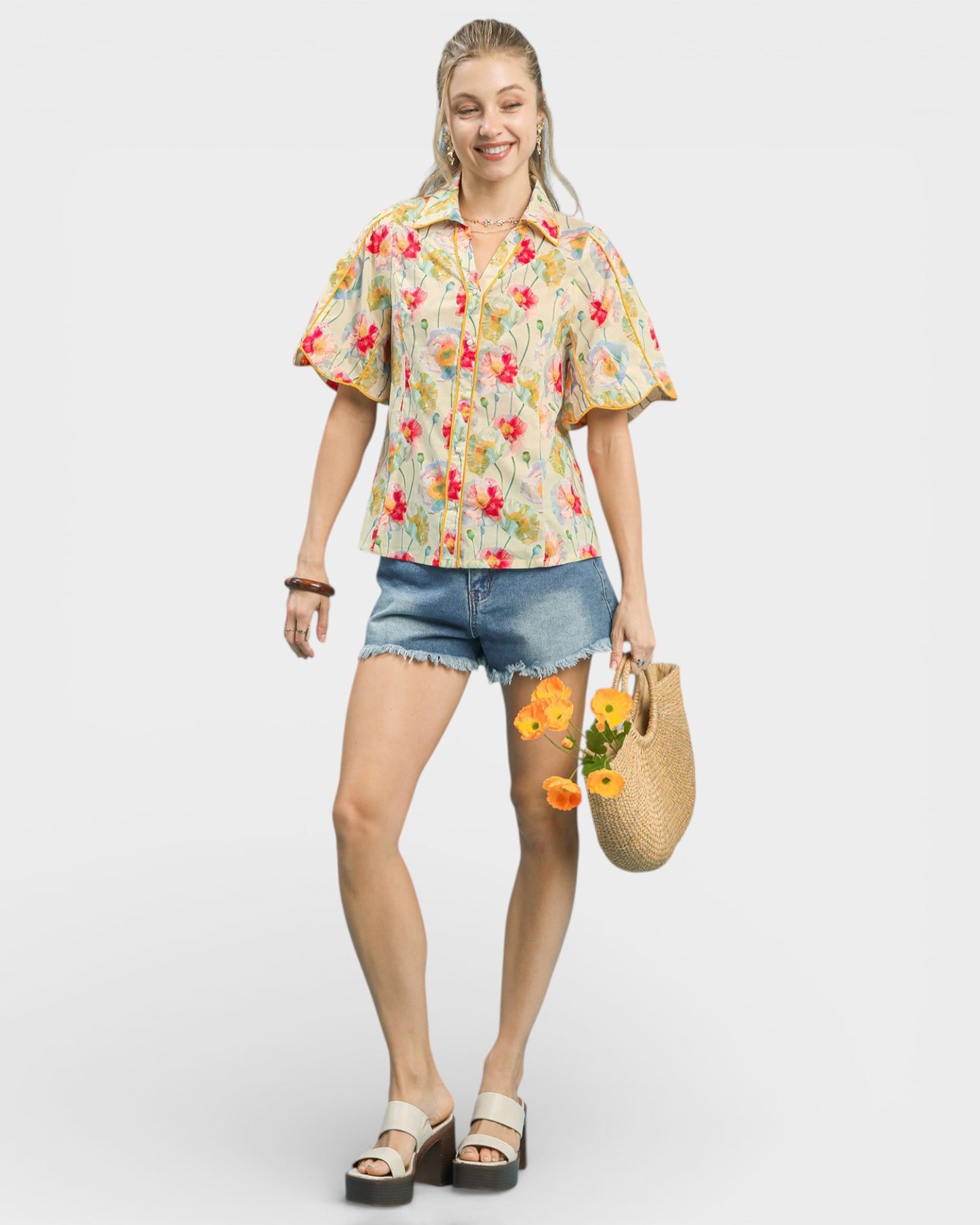 Woman wearing a floral shirt and denim shorts, holding flowers and a straw bag on a white background