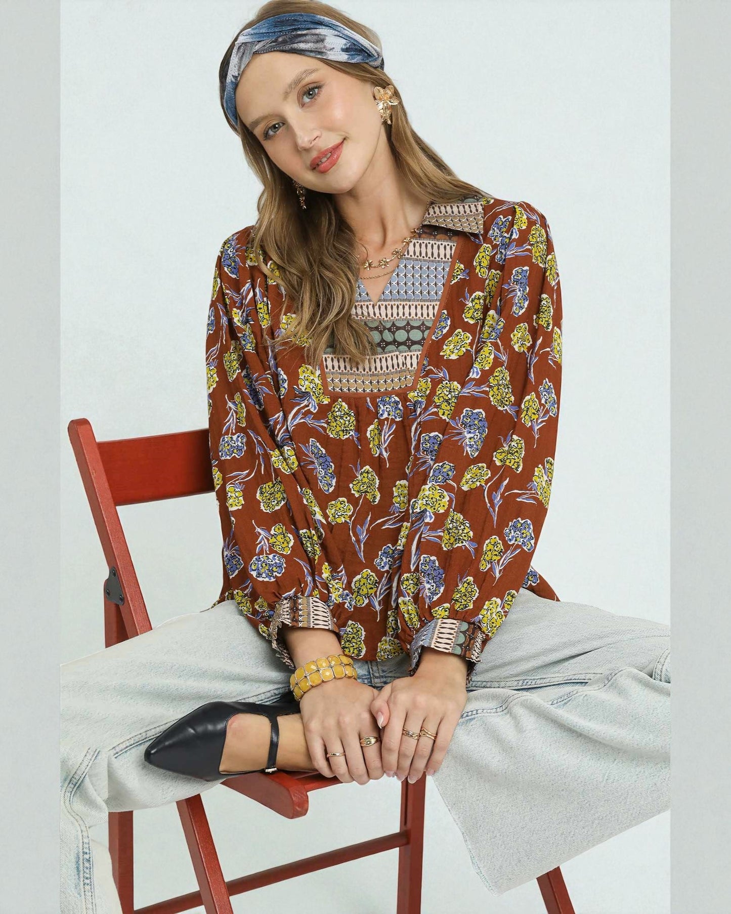 Woman sitting on a red chair wearing a patterned blouse and jeans.