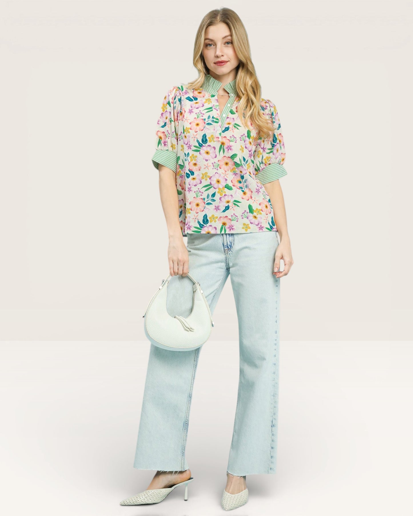 Woman wearing a floral blouse and light blue jeans, holding a matching handbag on a white background