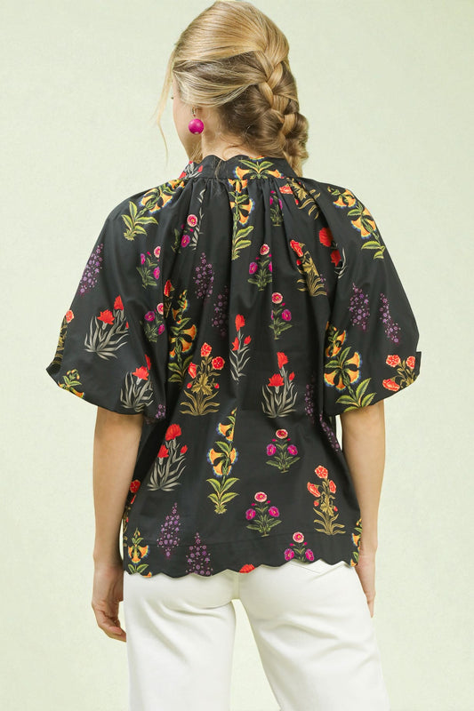 Person wearing a black floral blouse with white pants on a light green background