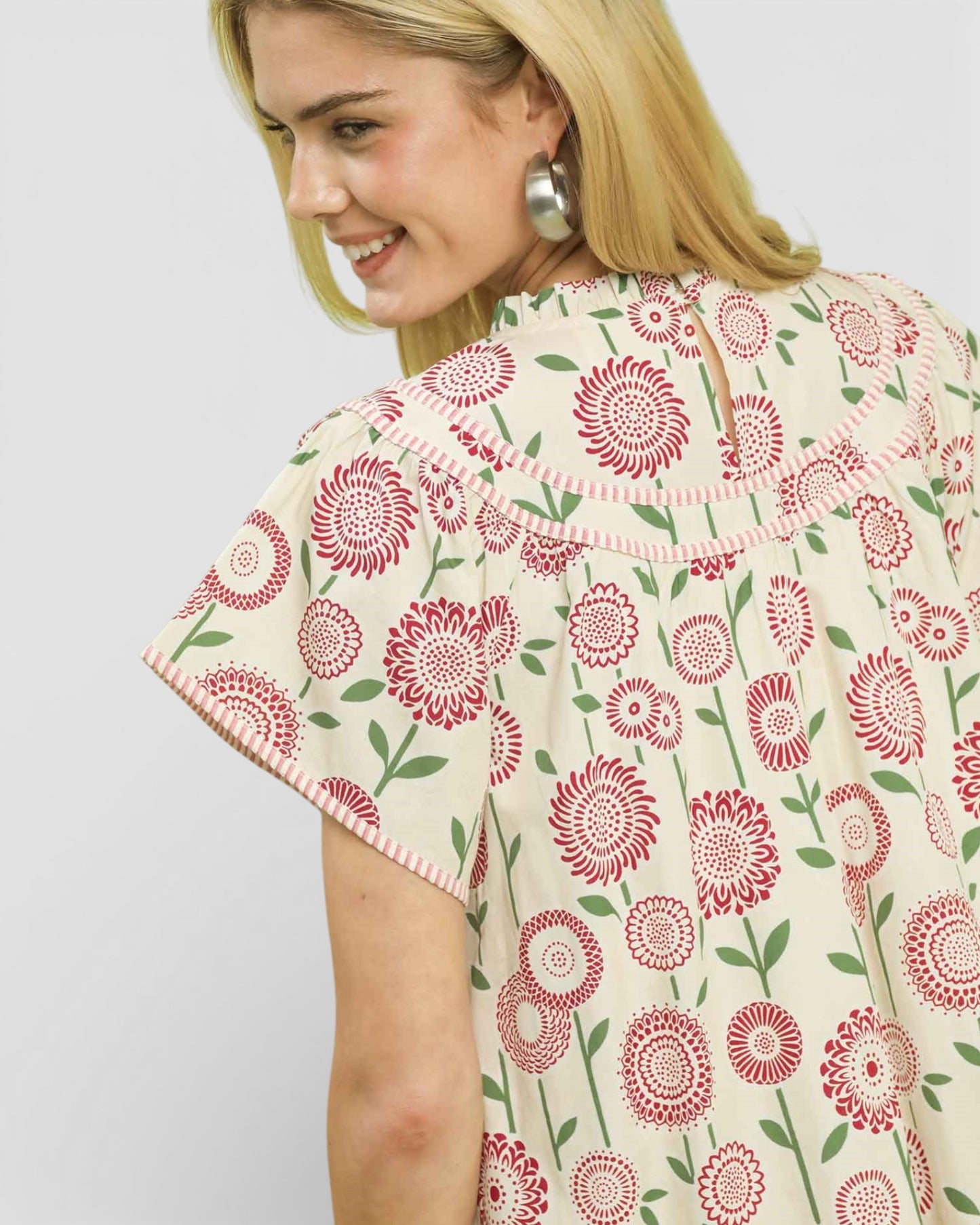 Woman wearing a floral patterned top with red flowers on a white background