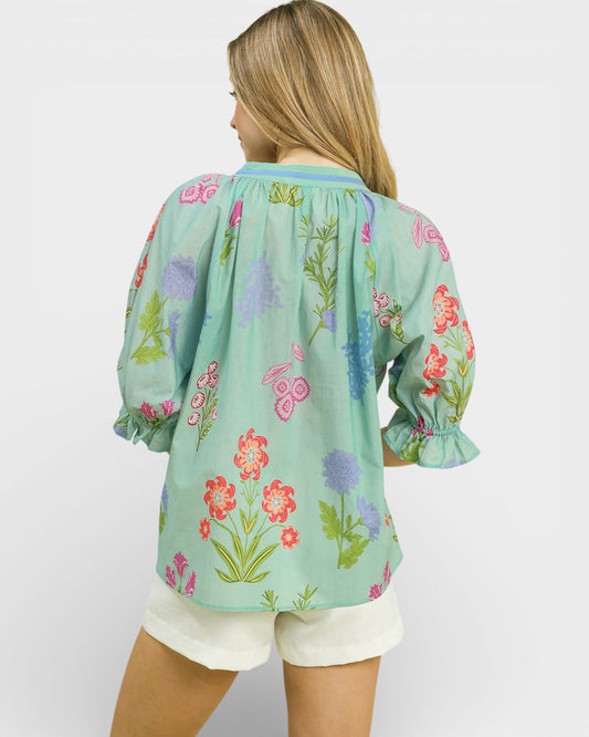 Woman wearing a light blue floral blouse with white shorts on a plain background