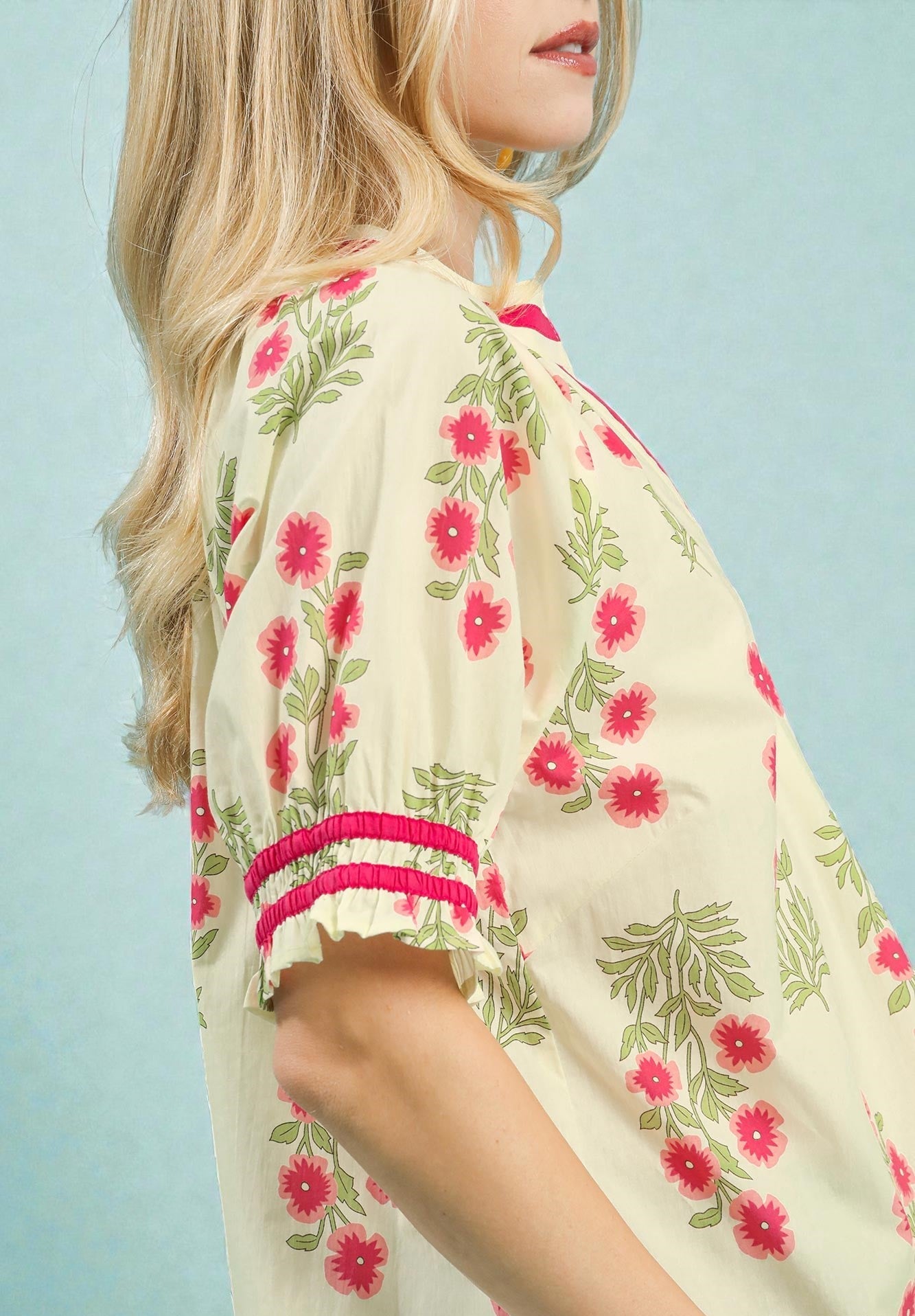 Woman wearing a floral kimono-style garment with pink flowers and green leaves on a light blue background.