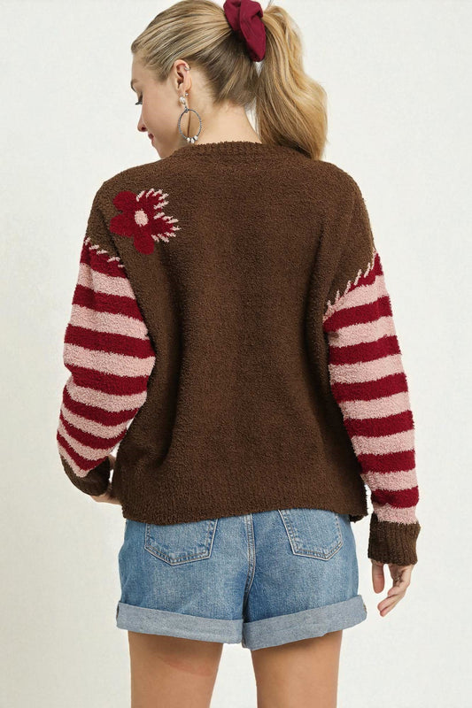 Person wearing a brown sweater with red and white pattern, standing against a plain background