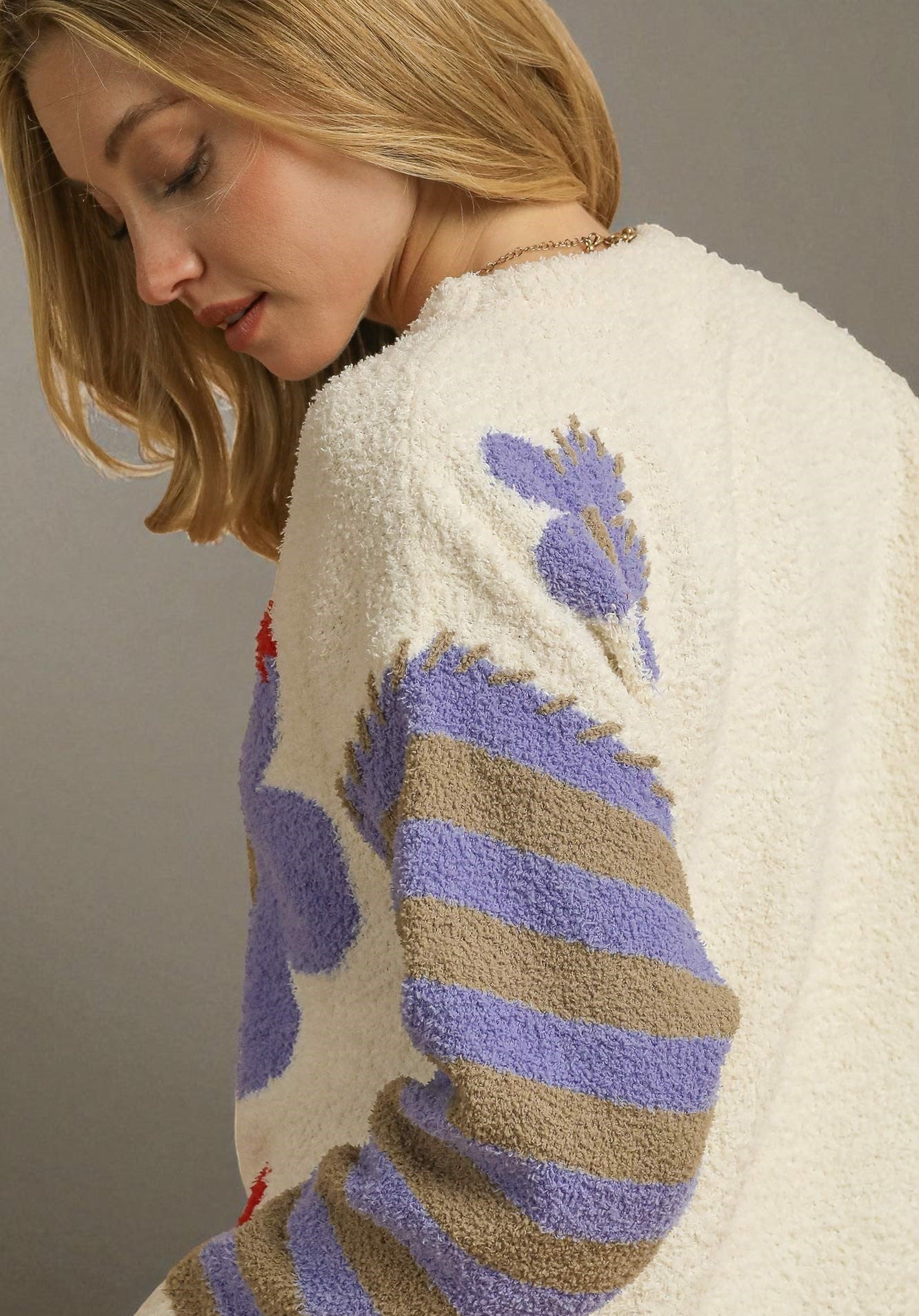 Woman wearing a cream sweater with colorful patterns on a plain background