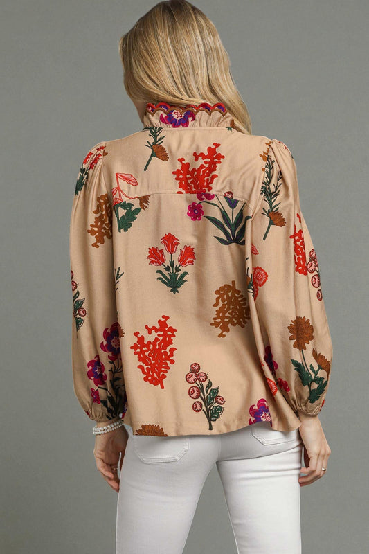 Woman wearing a beige blouse with colorful floral embroidery on a gray background