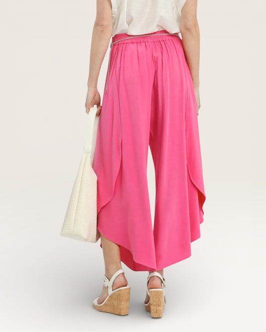 Person wearing bright pink wide-leg pants with a white top and sandals on a light background