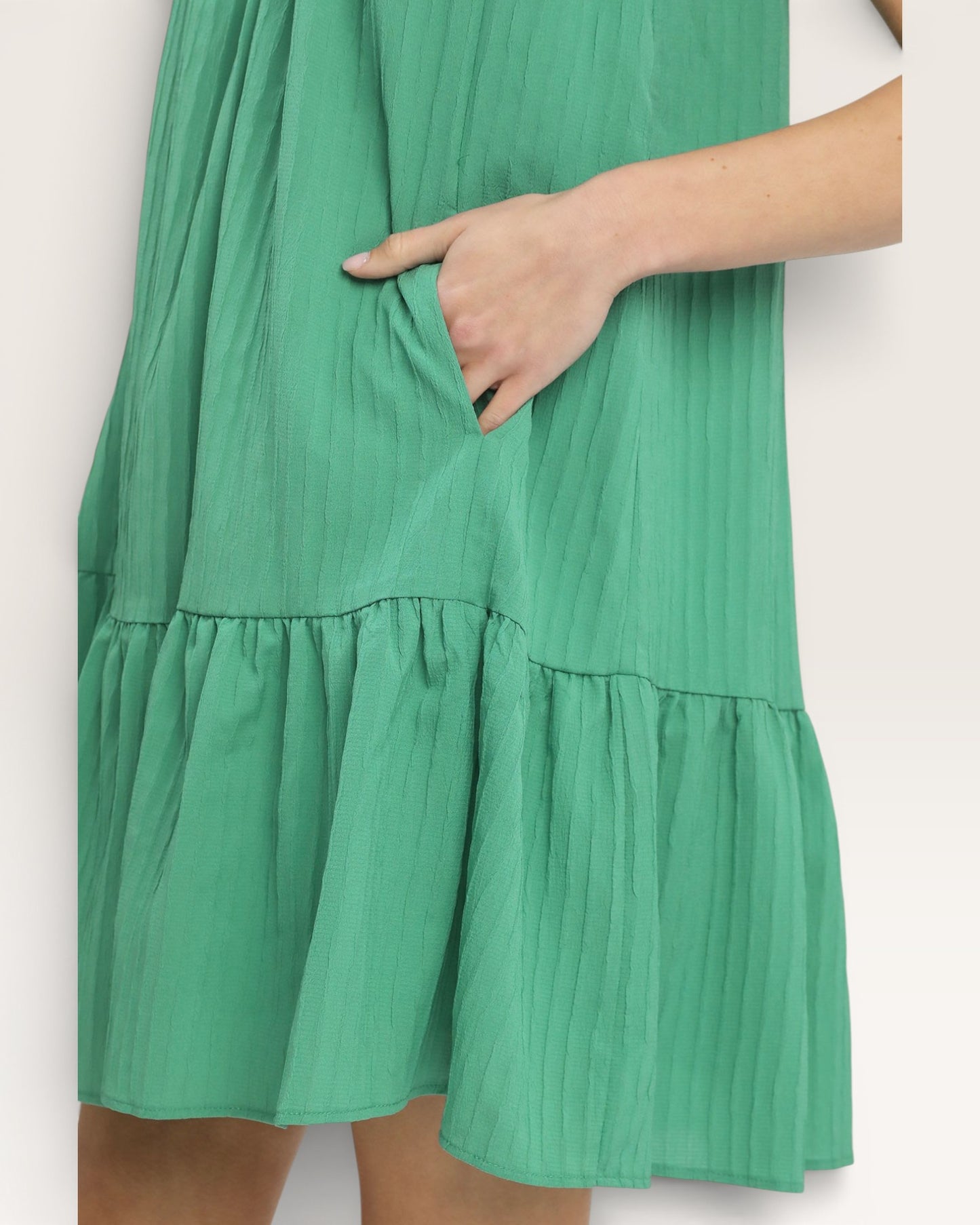 Green dress with tiered skirt and a hand in the pocket on a white background
