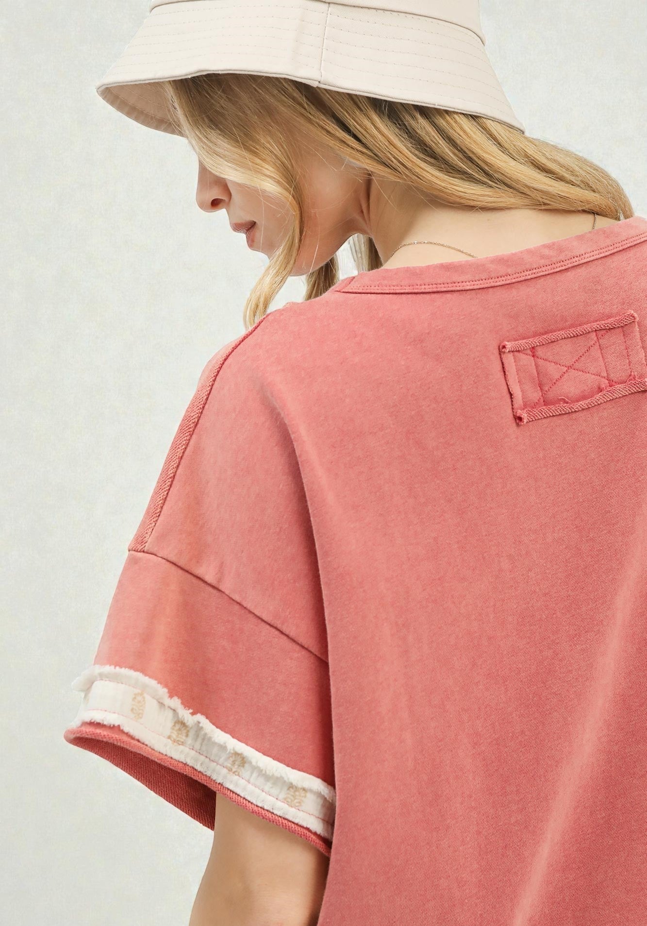 Person wearing a pink t-shirt with a visible brand logo on a plain background