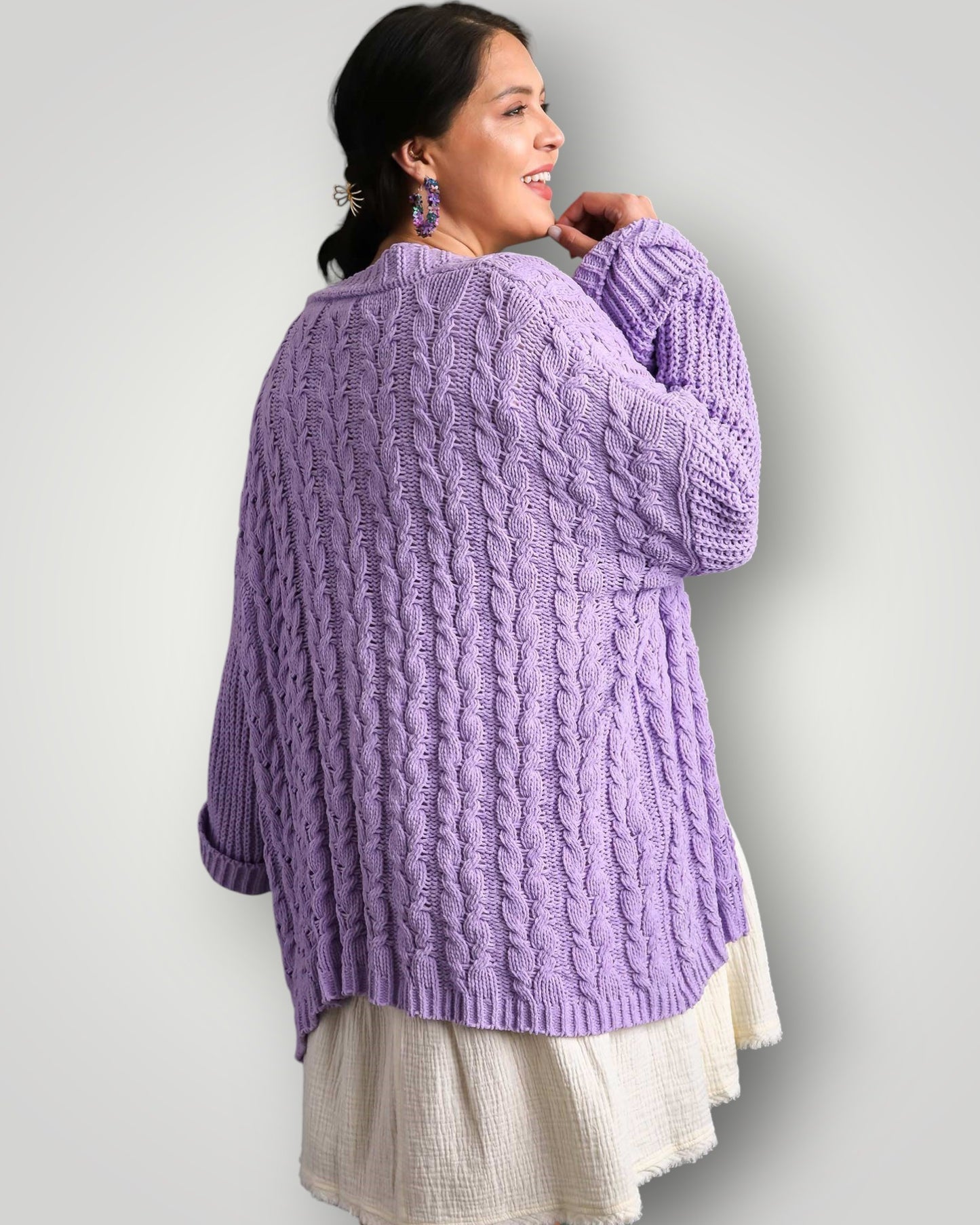 Woman wearing a purple cable knit sweater against a plain background