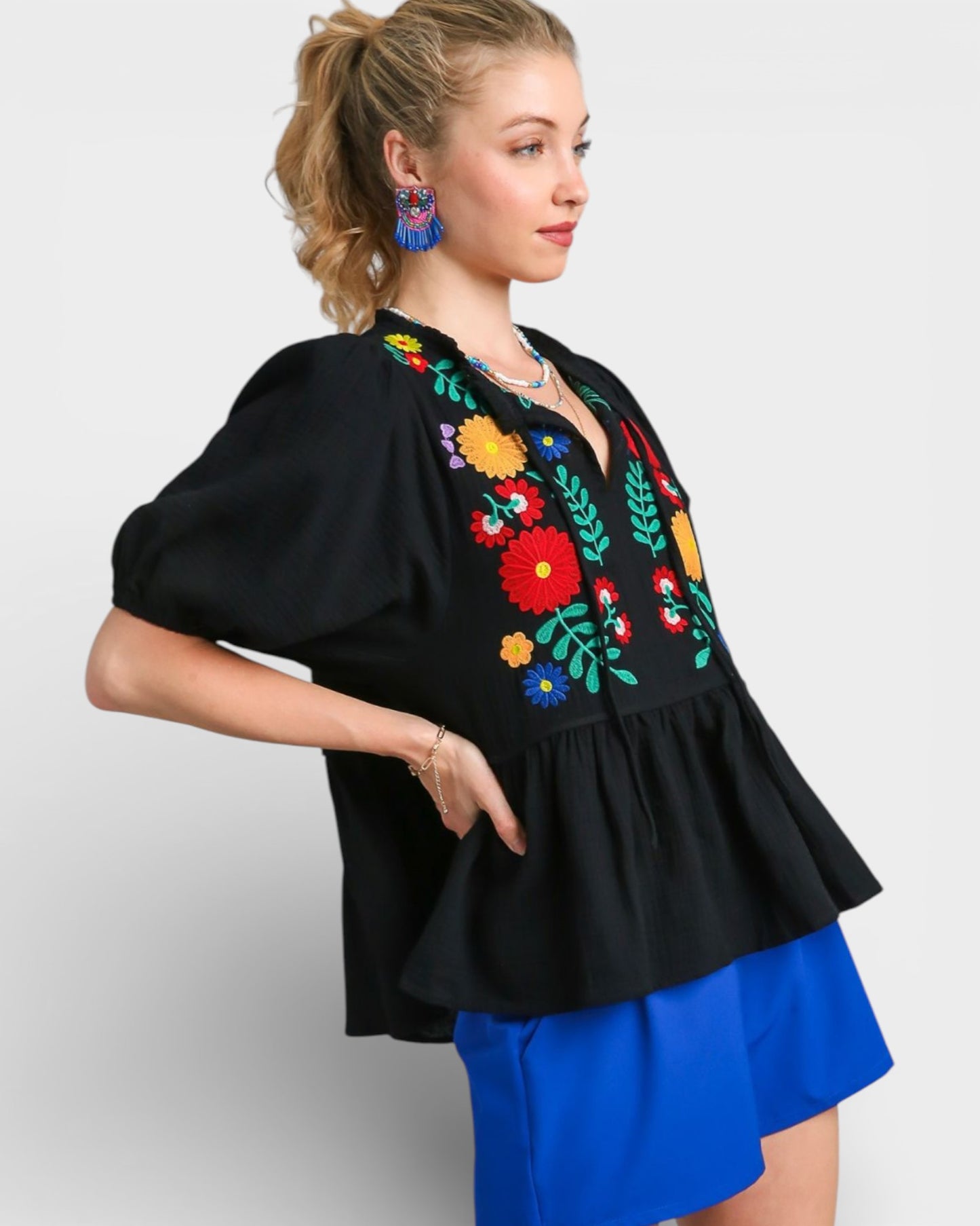 Woman wearing a black blouse with colorful floral embroidery and a blue skirt on a white background