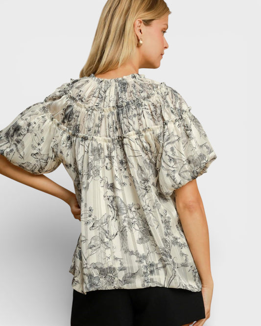 Woman wearing a floral blouse with puffed sleeves on a plain background