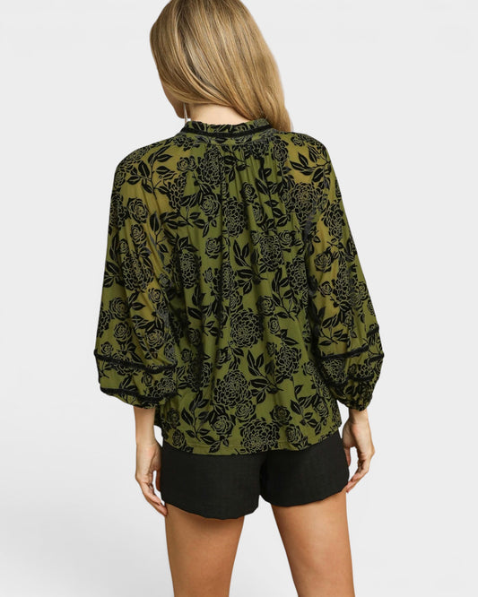 Person wearing a green patterned blouse and black shorts on a white background